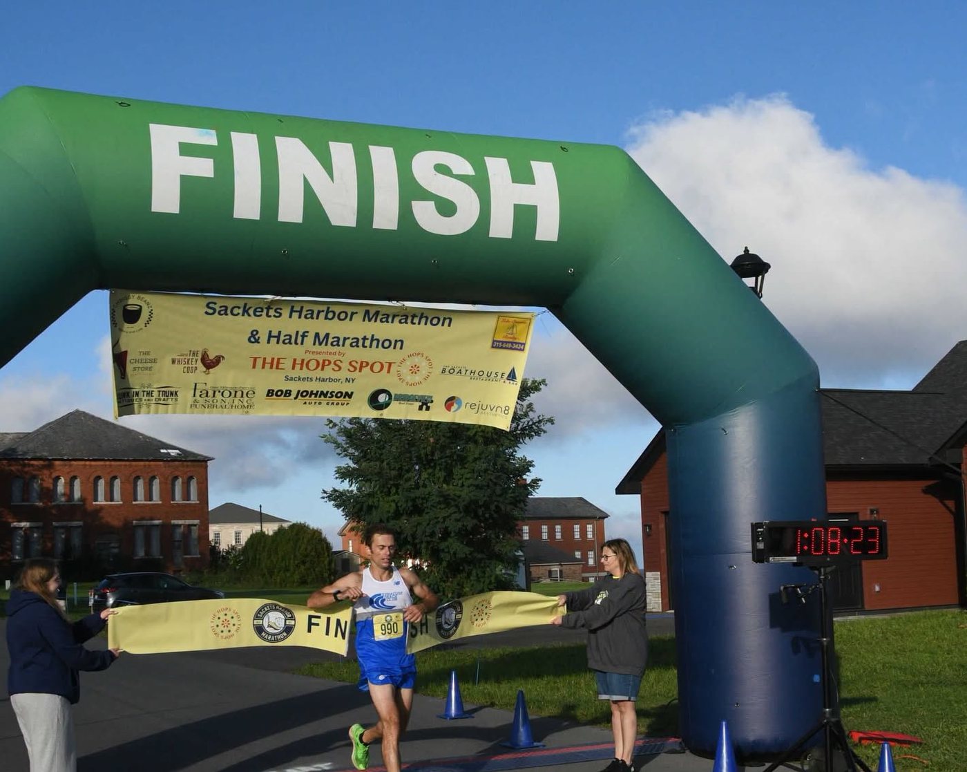 Sam Morse breaking the finish tape under the FINISH arch, the race clock reading 1:08:23