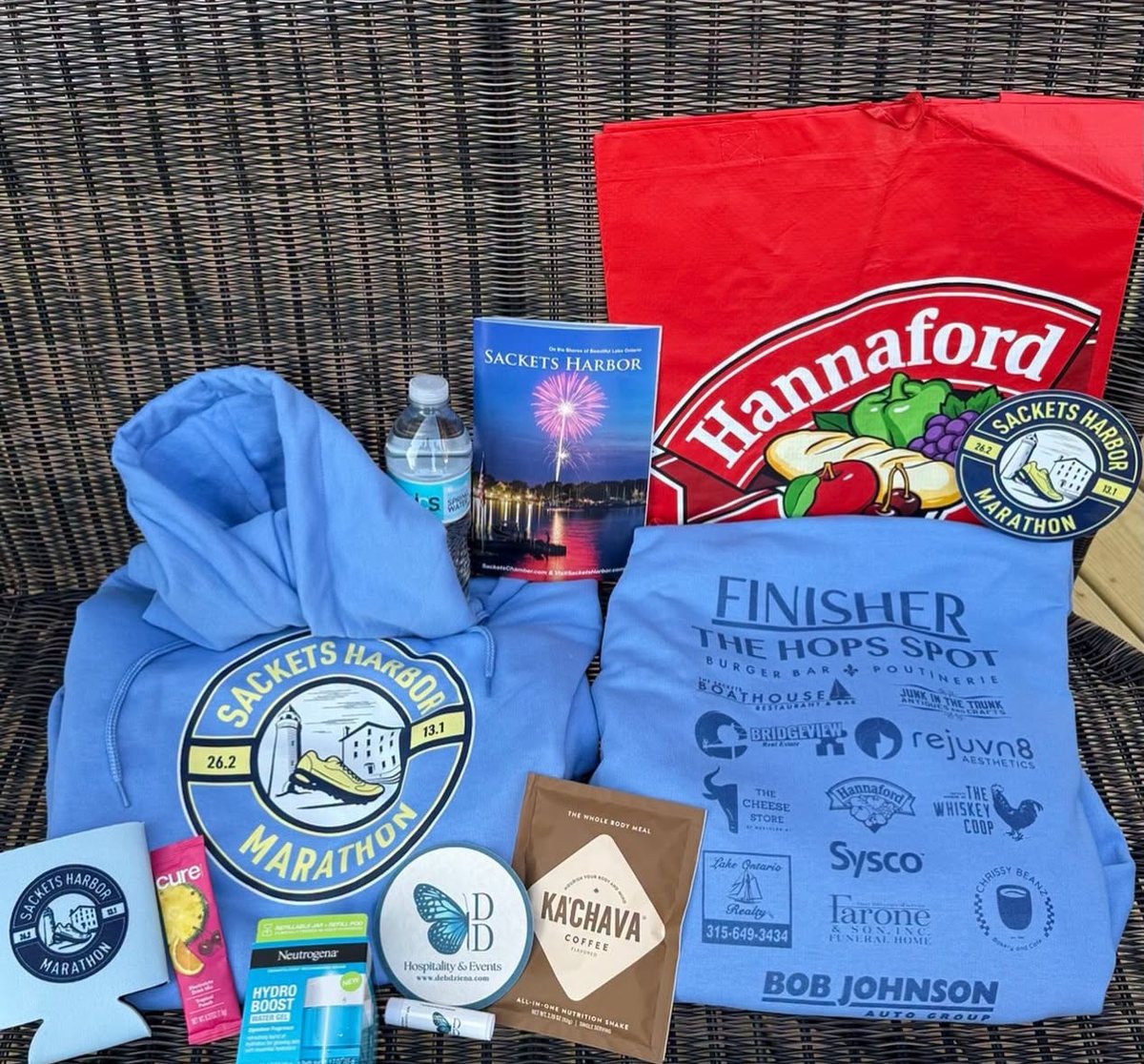 A goody bag laid out: the finisher hoodie, a koozie, a logo sticker, coffee and samples