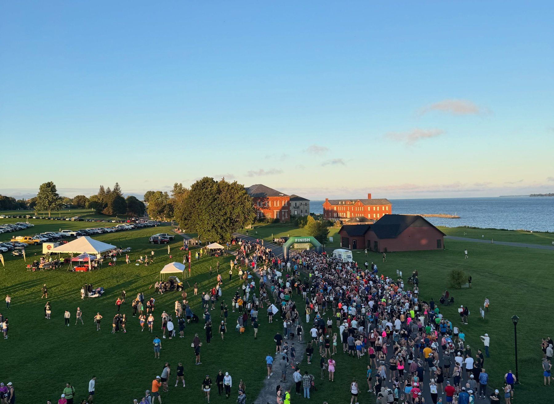 Aerial view of the start area at dawn: runners gathered on the polo fields with Madison Barracks and Lake Ontario behind