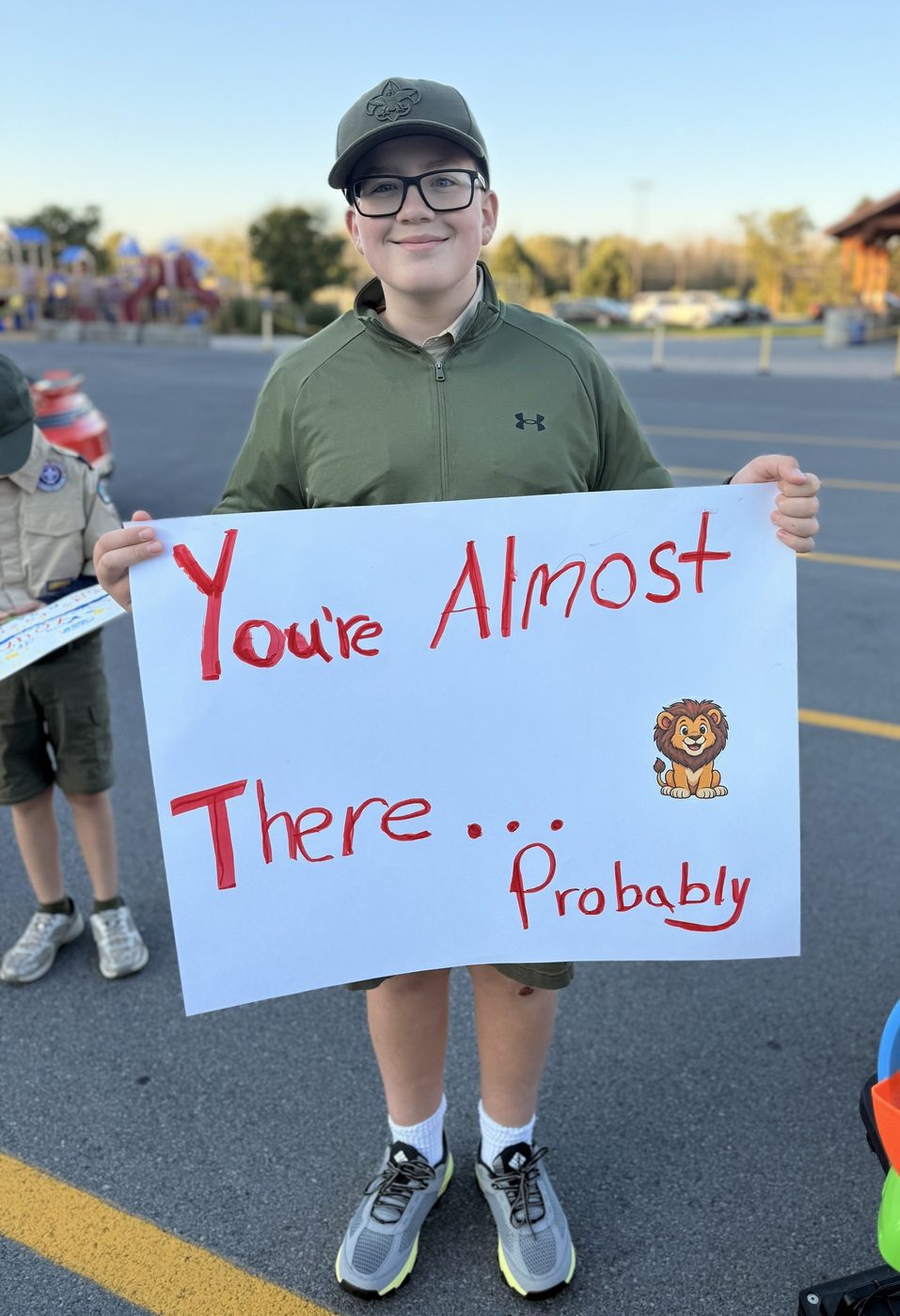 A young spectator holding a sign reading You're Almost There... Probably