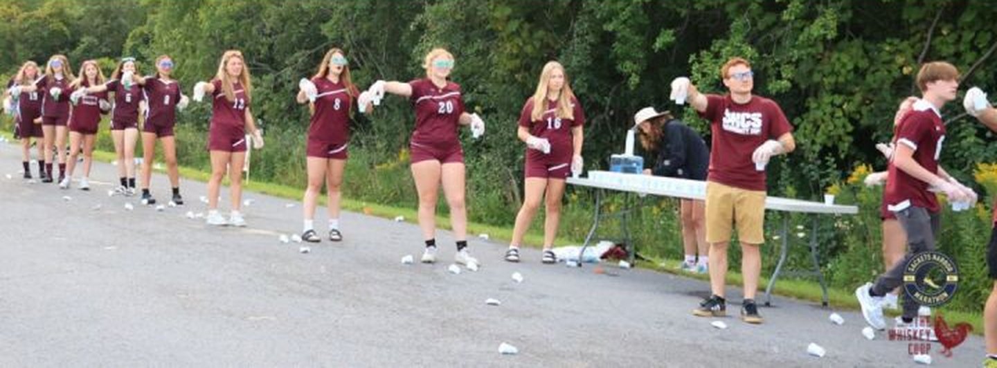 A line of volunteers in matching jerseys holding out cups of water to runners